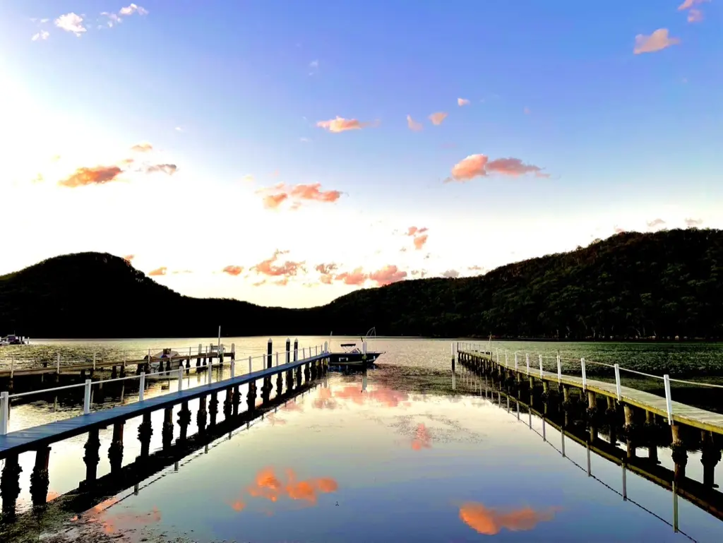 Jetty, floating pontoon and boat reflected in the bay at sunset