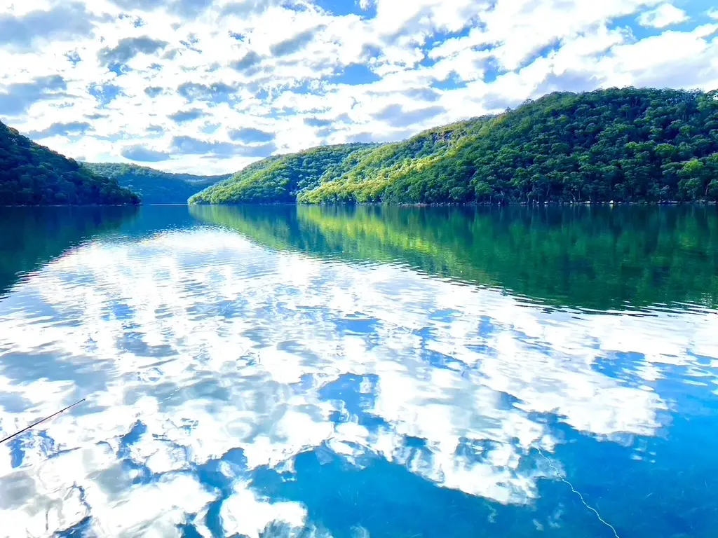 Clouds and bushland reflected in calm Woy Woy Bay